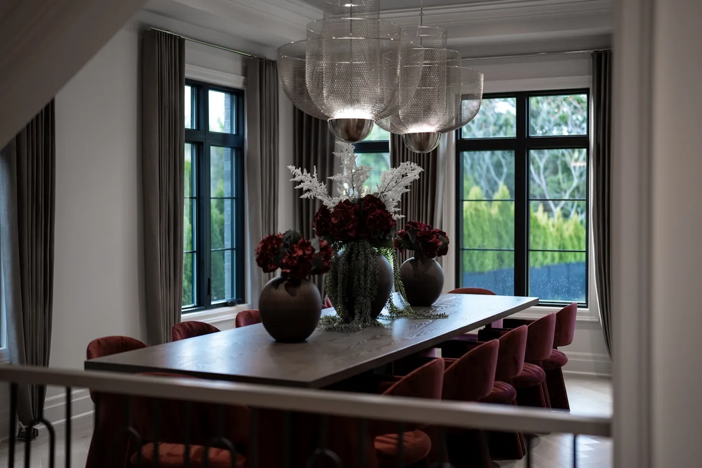 Elegant dining room with tall drapes, a chandelier and deep red chairs