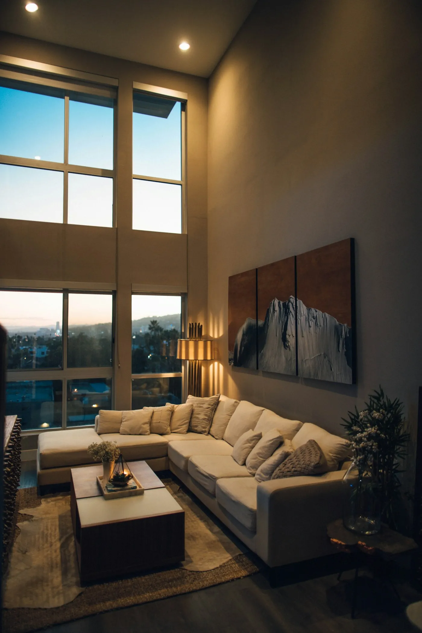 Living room at dusk with floor-to-ceiling windows and warm lamps